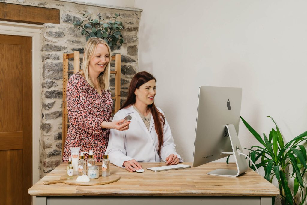 Women discussing skincare products in office setting.