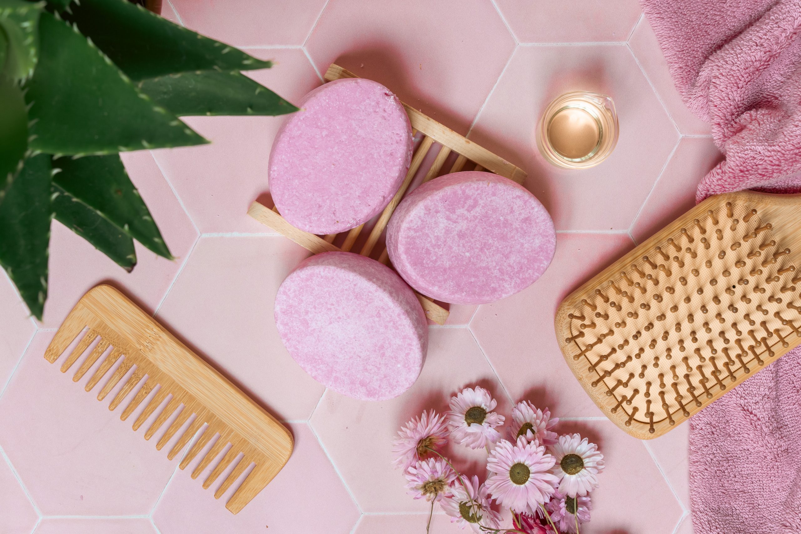 Pink shampoo bars, brush, flowers, and comb on tiles.