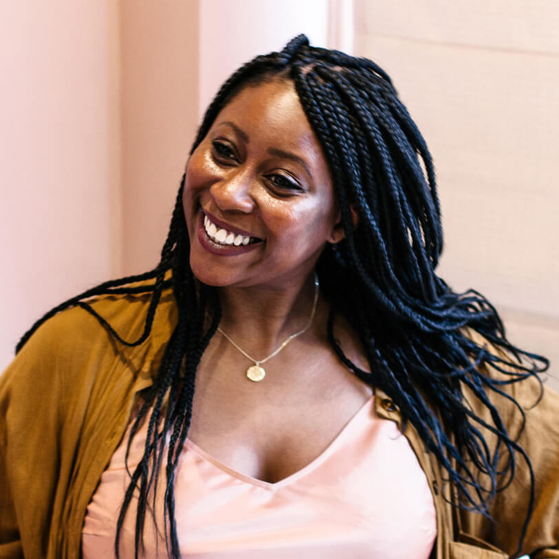 Smiling person with braided hair in casual outfit.