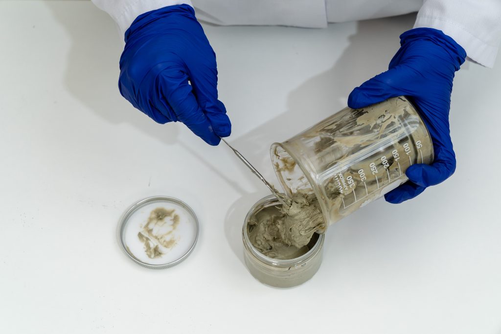 Gloved hands handling wet cement in laboratory jars.