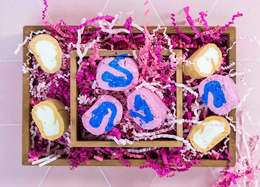 Colorful bath bombs in wooden box with pink confetti.