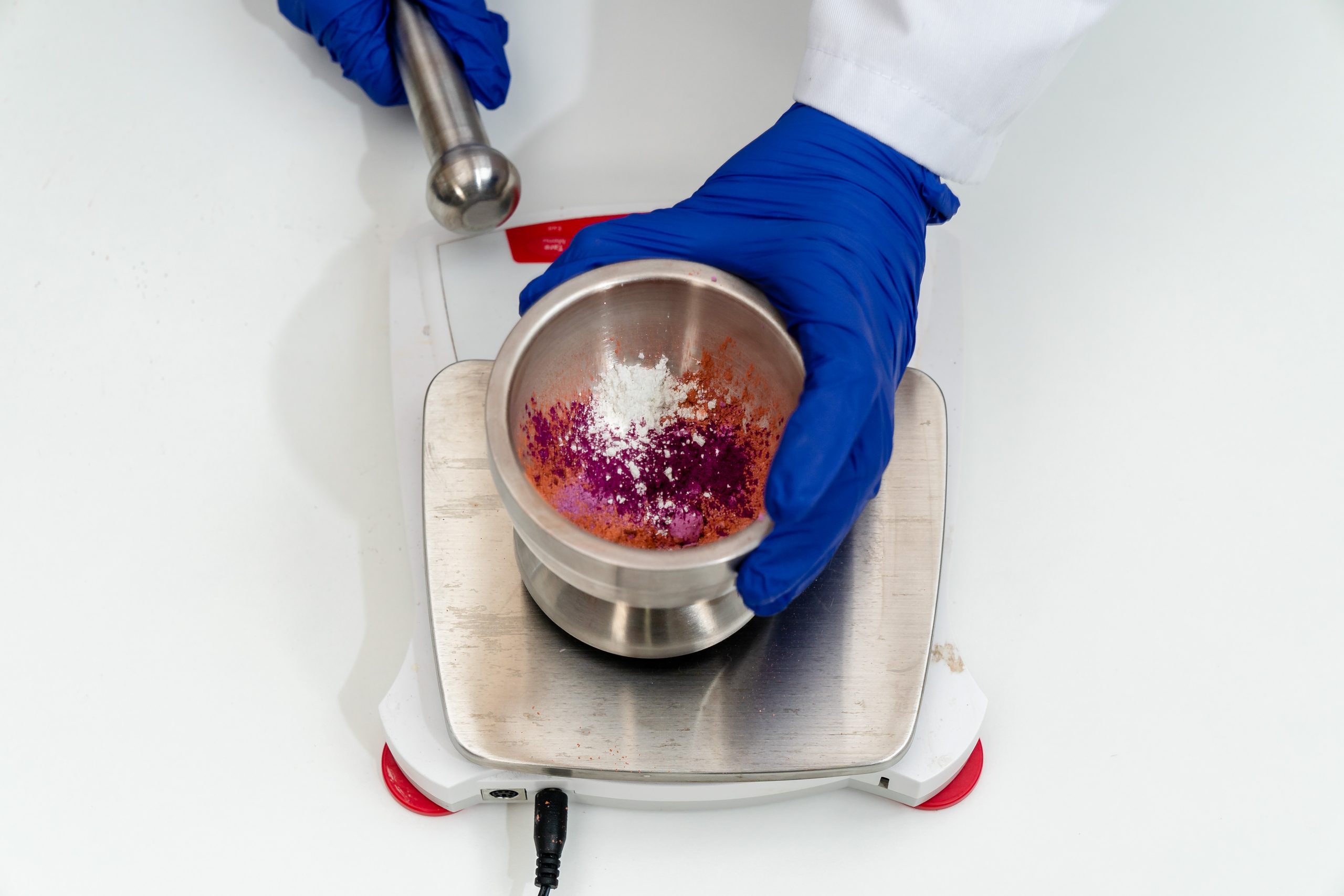 Mixing colorful powders in laboratory with pestle and mortar.