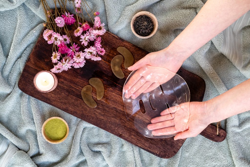 Hands holding transparent face mask, spa accessories nearby.