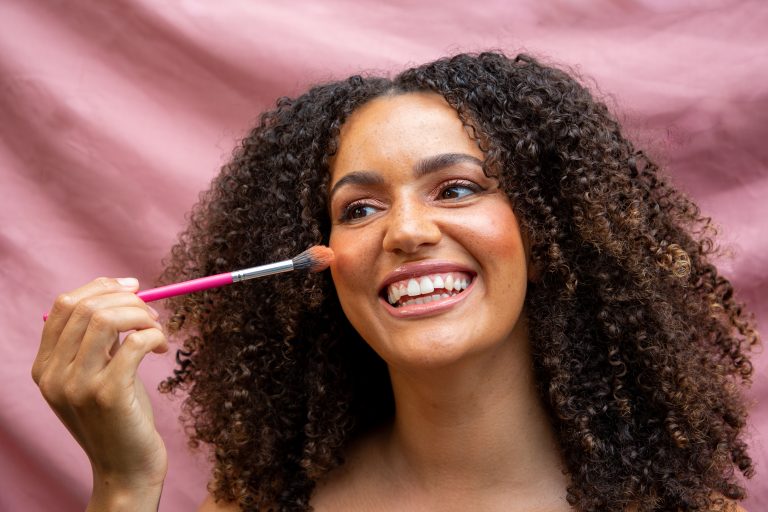 Smiling woman applying makeup with a brush