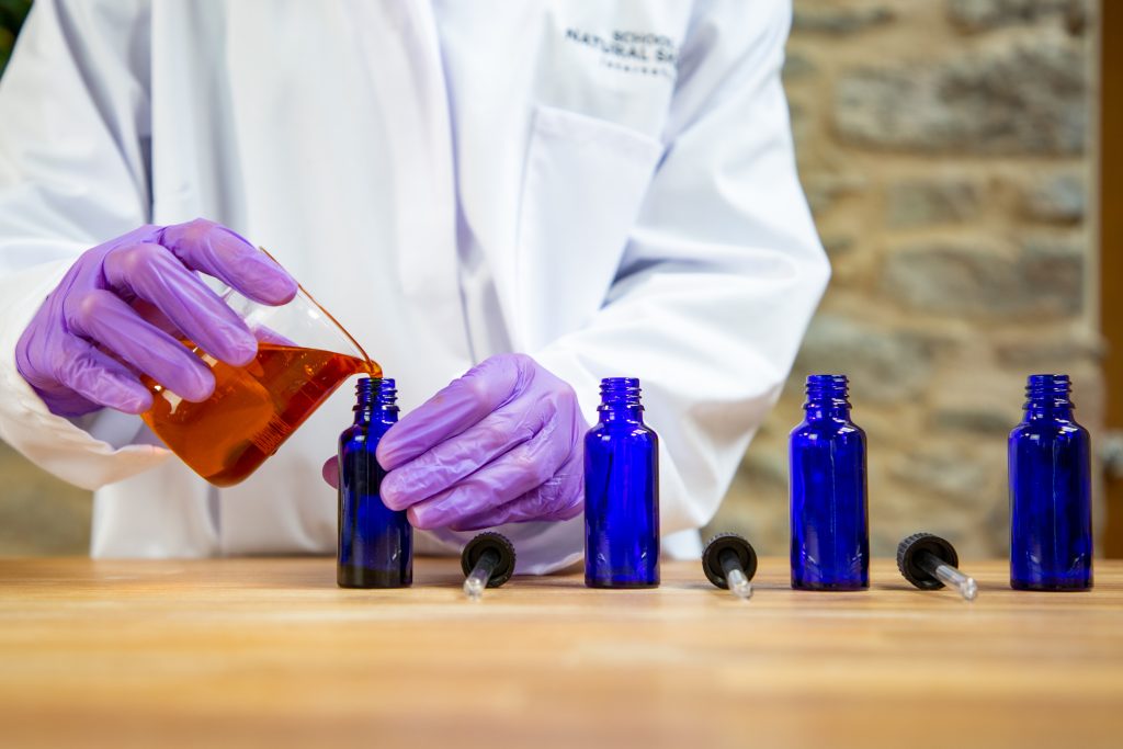 Scientist pouring liquid into blue glass bottles.