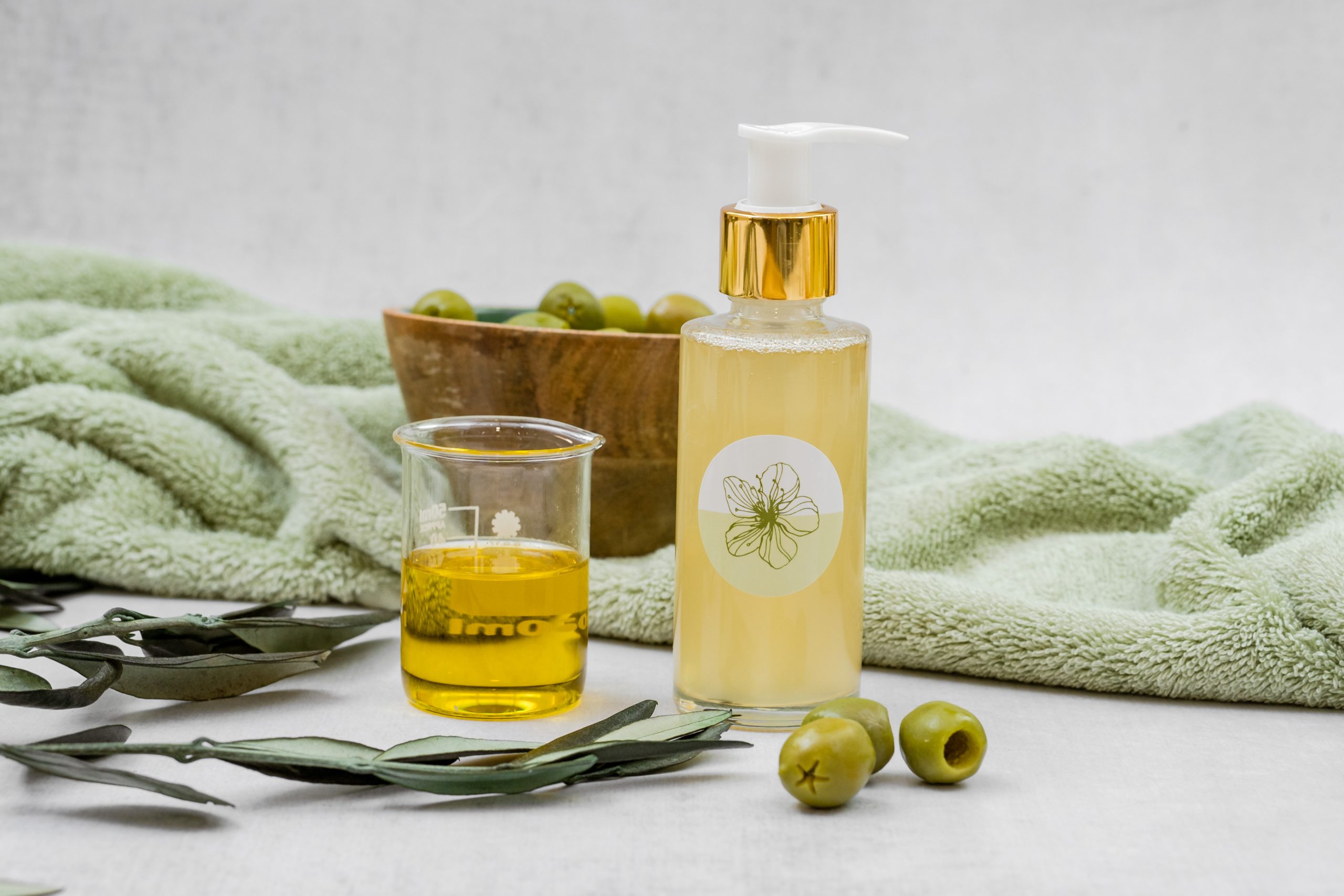 Olive oil and skincare products on green towel.