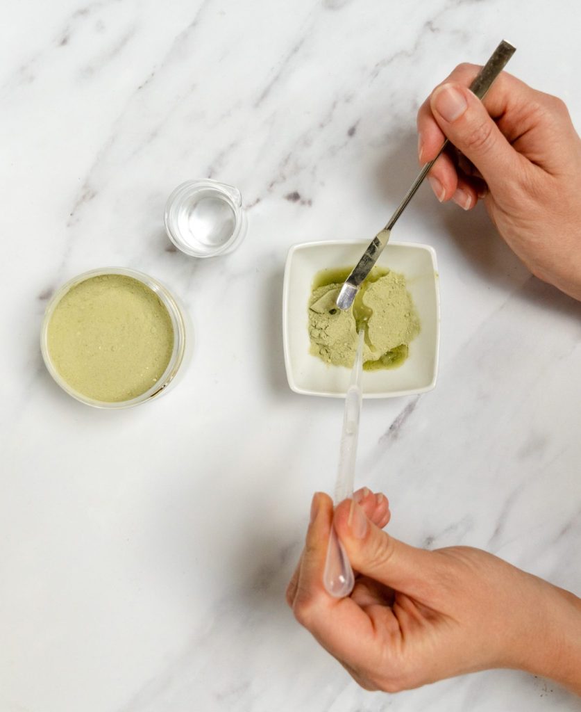 Mixing green powder with liquid on marble surface.