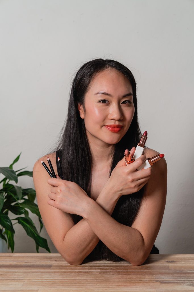 Woman holding lipsticks and pencils with plants in background.