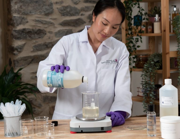 Woman in lab coat pouring liquid into beaker.