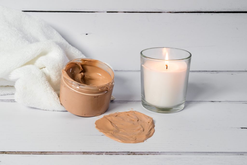 Face cream and candle on white surface