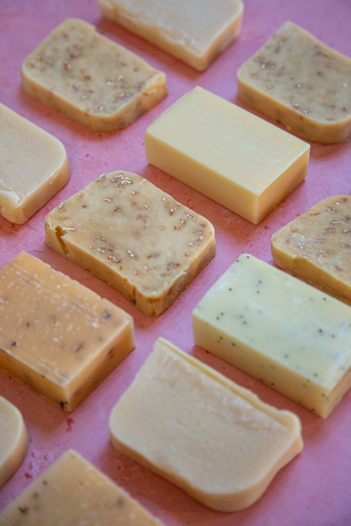 Assorted handmade soap bars on pink background.