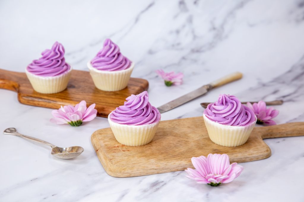 Purple frosted cupcakes on wooden boards with flowers.