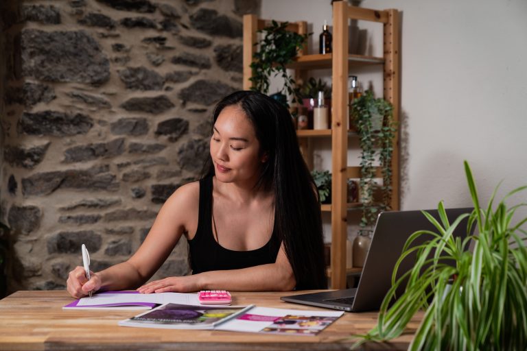 Woman writing at desk with laptop and books