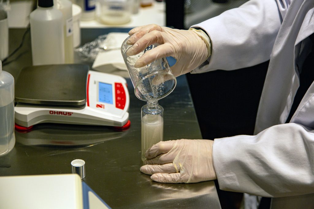 Scientist pours powder in laboratory beaker.