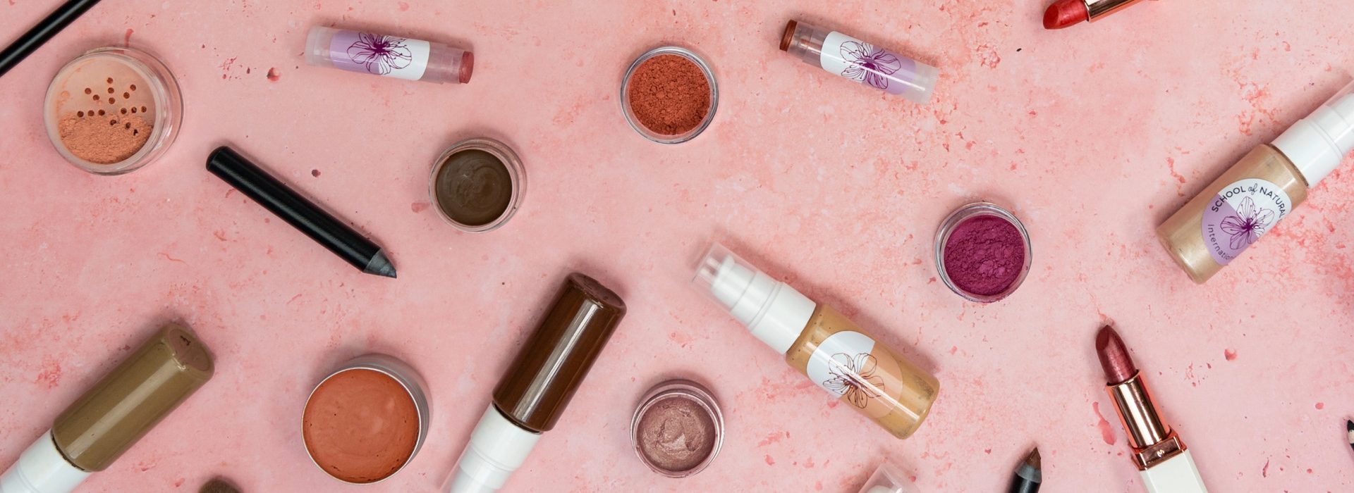 Assorted natural makeup products on pink background.