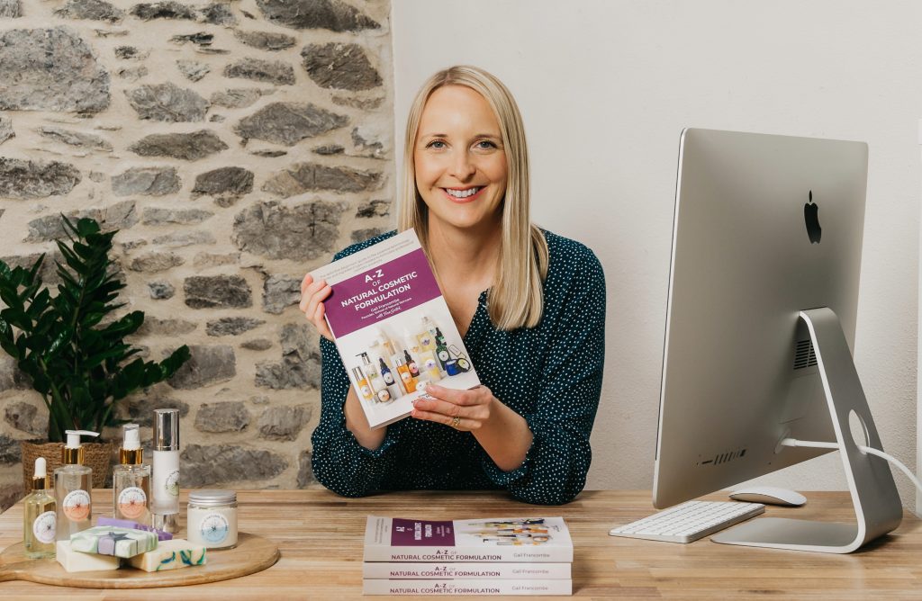 Smiling woman holding cosmetic formulation book at desk.