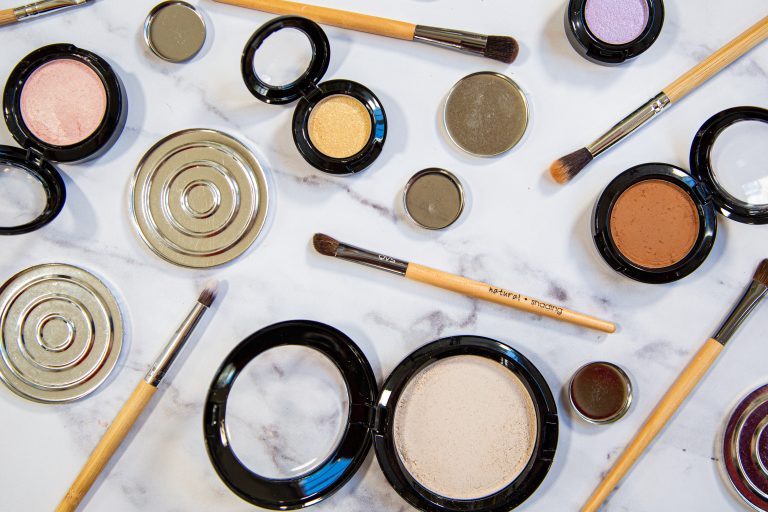 Flatlay of makeup products and brushes on marble surface.