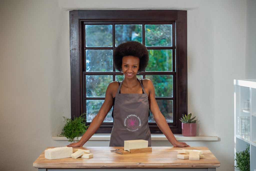 Woman in apron making soap by window.