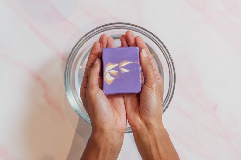 Hands holding purple artisan soap over bowl.