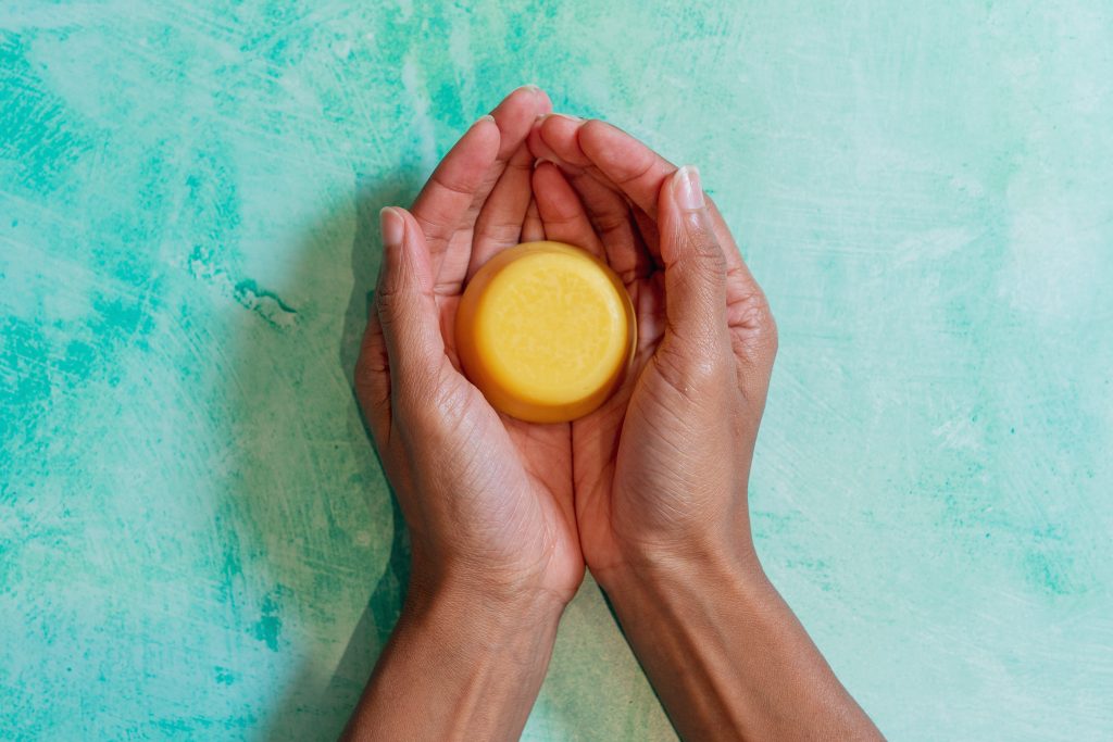 Hands holding a round yellow soap bar.