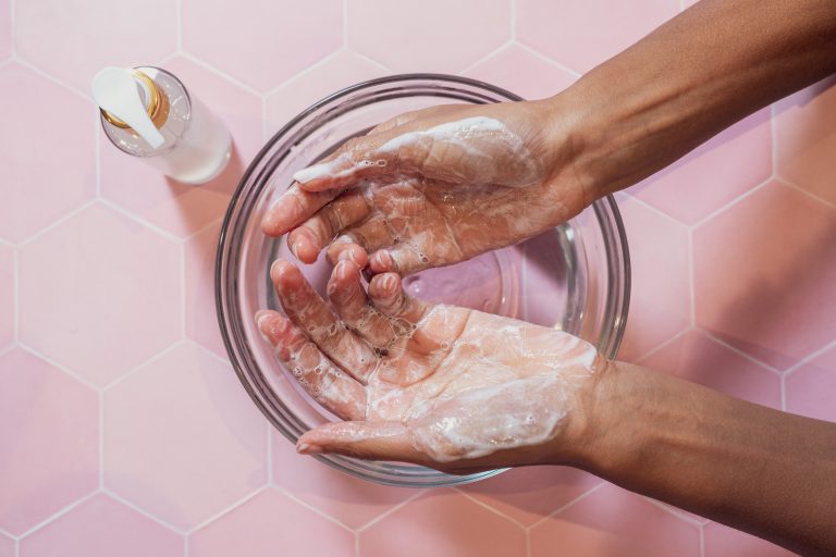 Hands washing with soap in bowl on pink tiles.