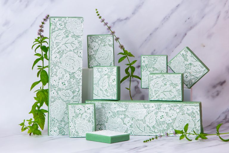 Lace-patterned green boxes with plants on marble background.