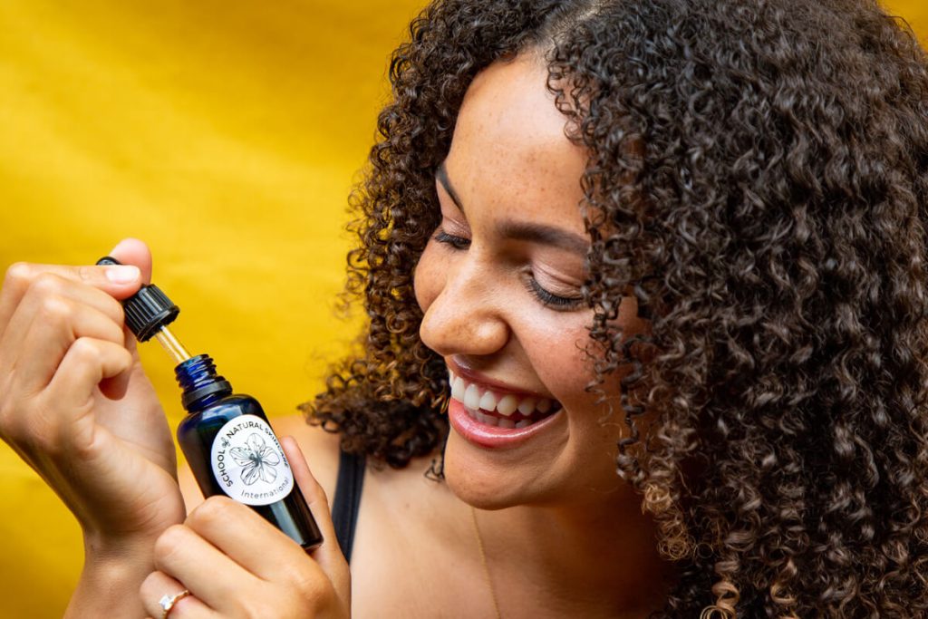 Smiling woman using skincare serum dropper bottle.