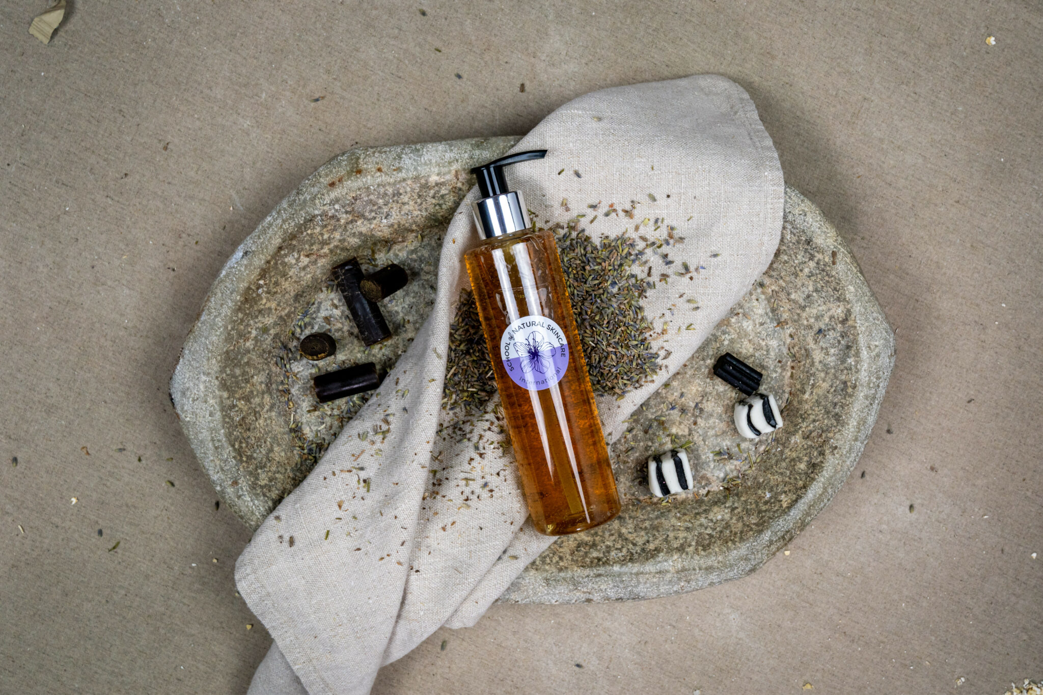 Natural skincare bottle with herbs on stone surface.