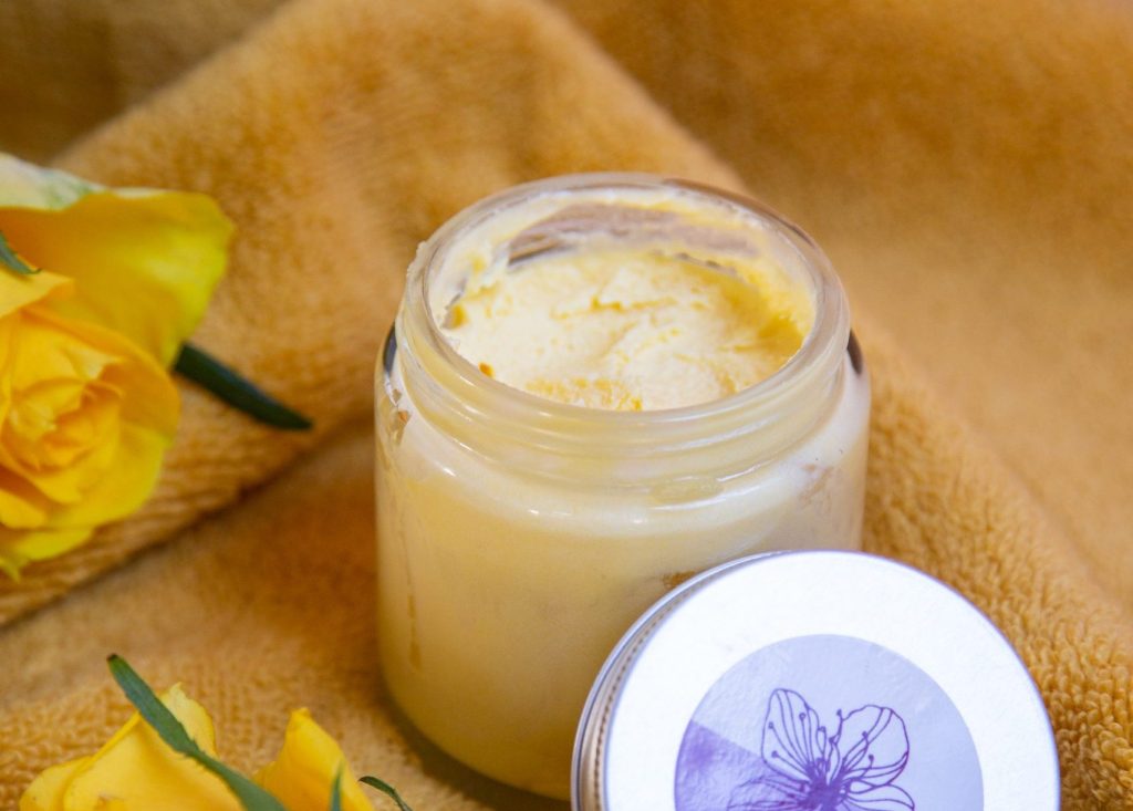 Glass jar of yellow body butter on towel.