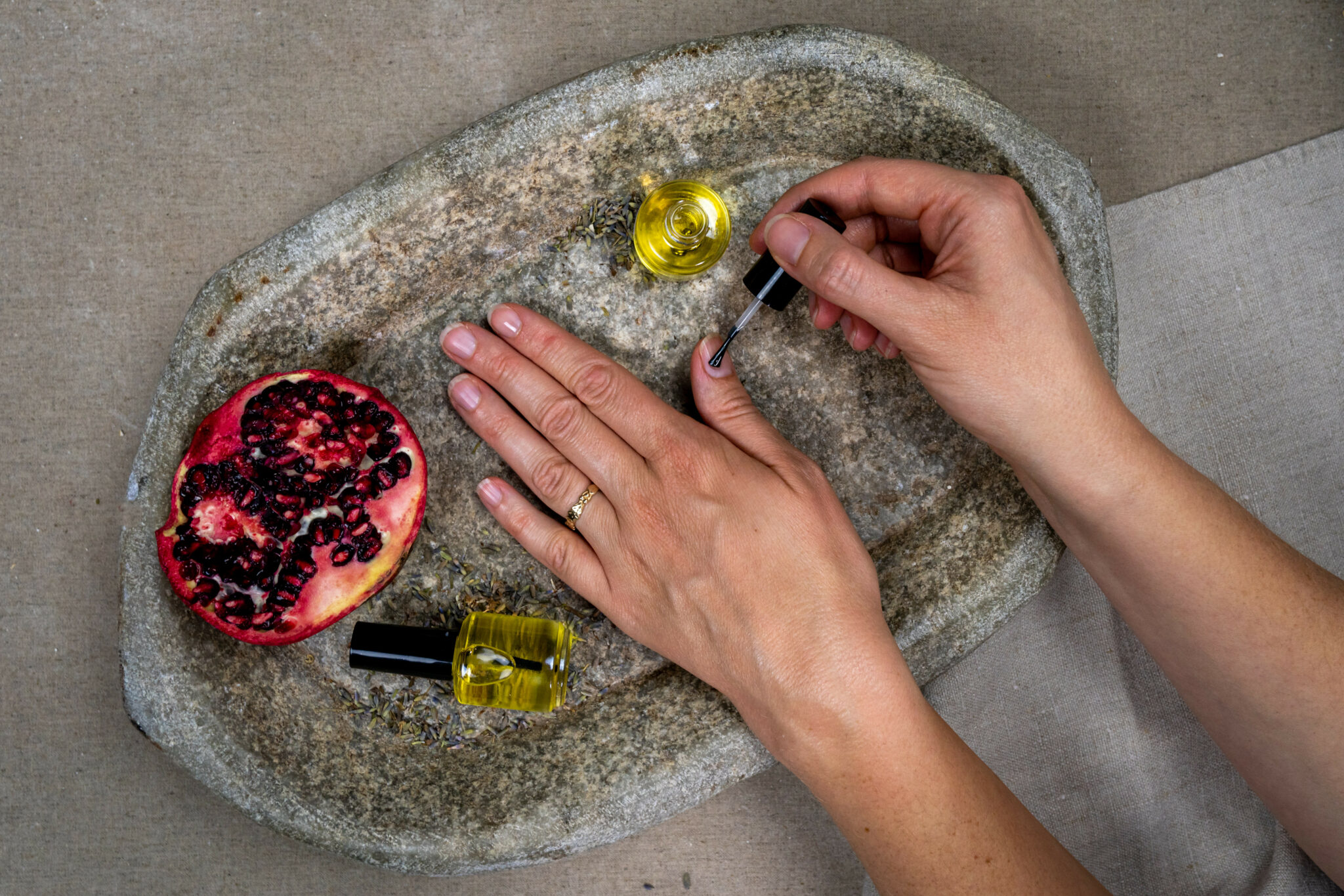 Applying nail polish beside pomegranate and oil bottle.