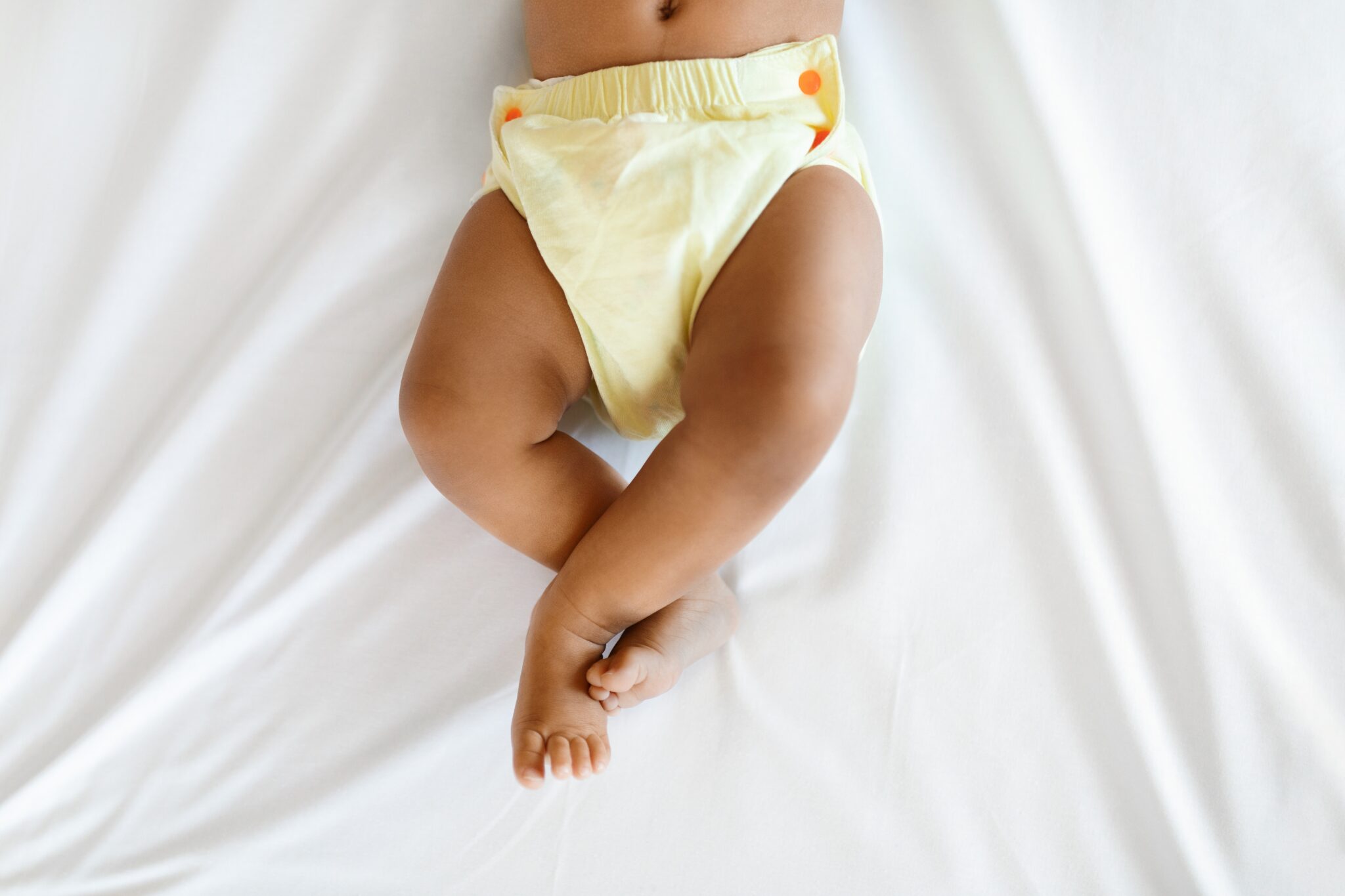 Baby wearing a yellow cloth diaper on bed.