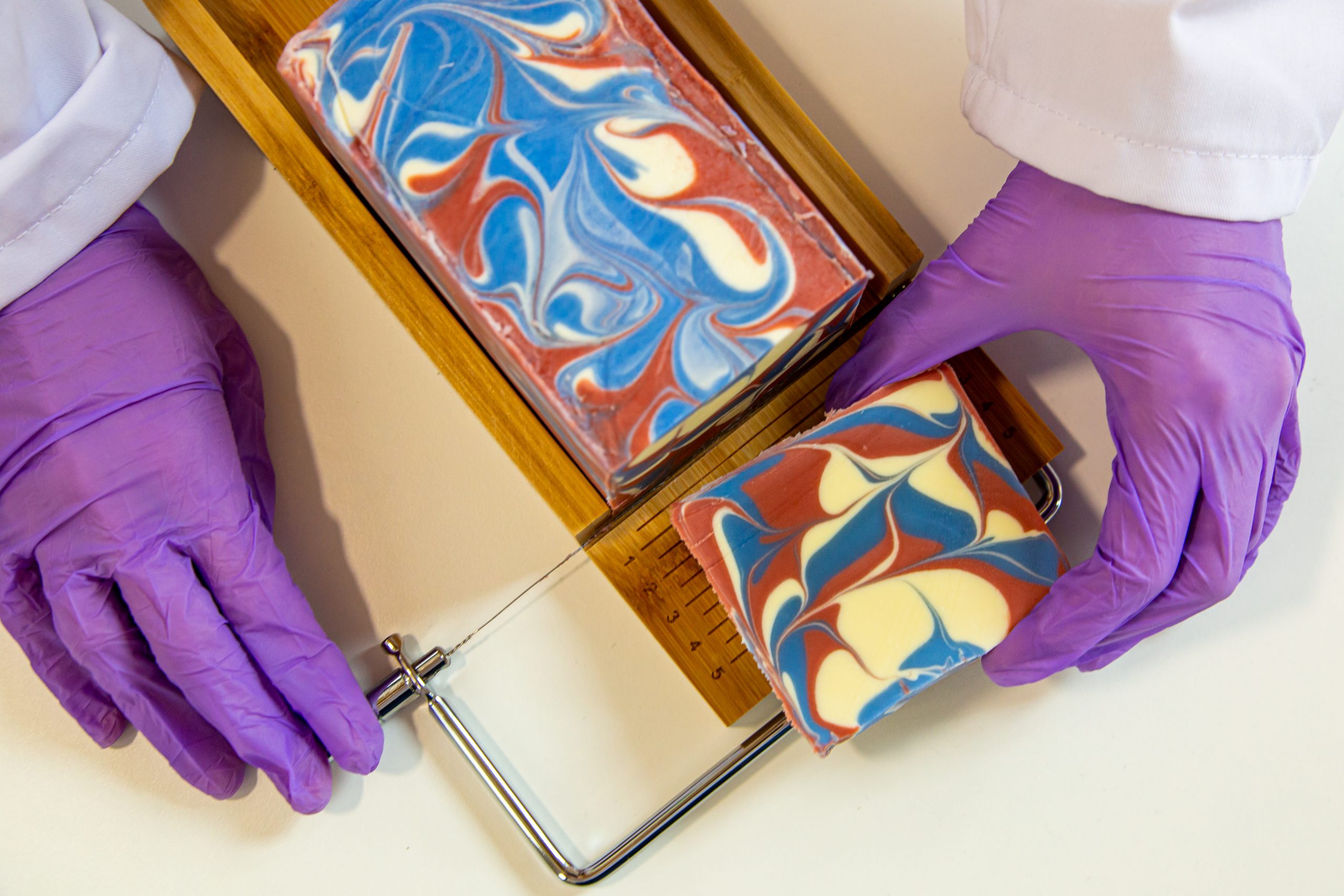 Person cutting colorful swirled soap with wire cutter