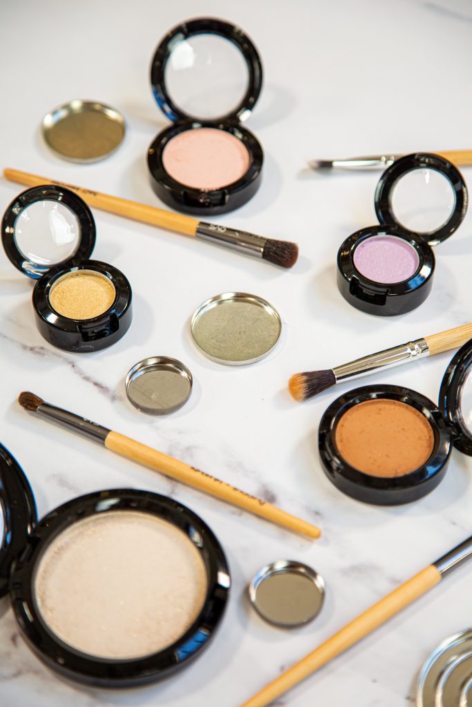 Assorted makeup products and brushes on white surface.