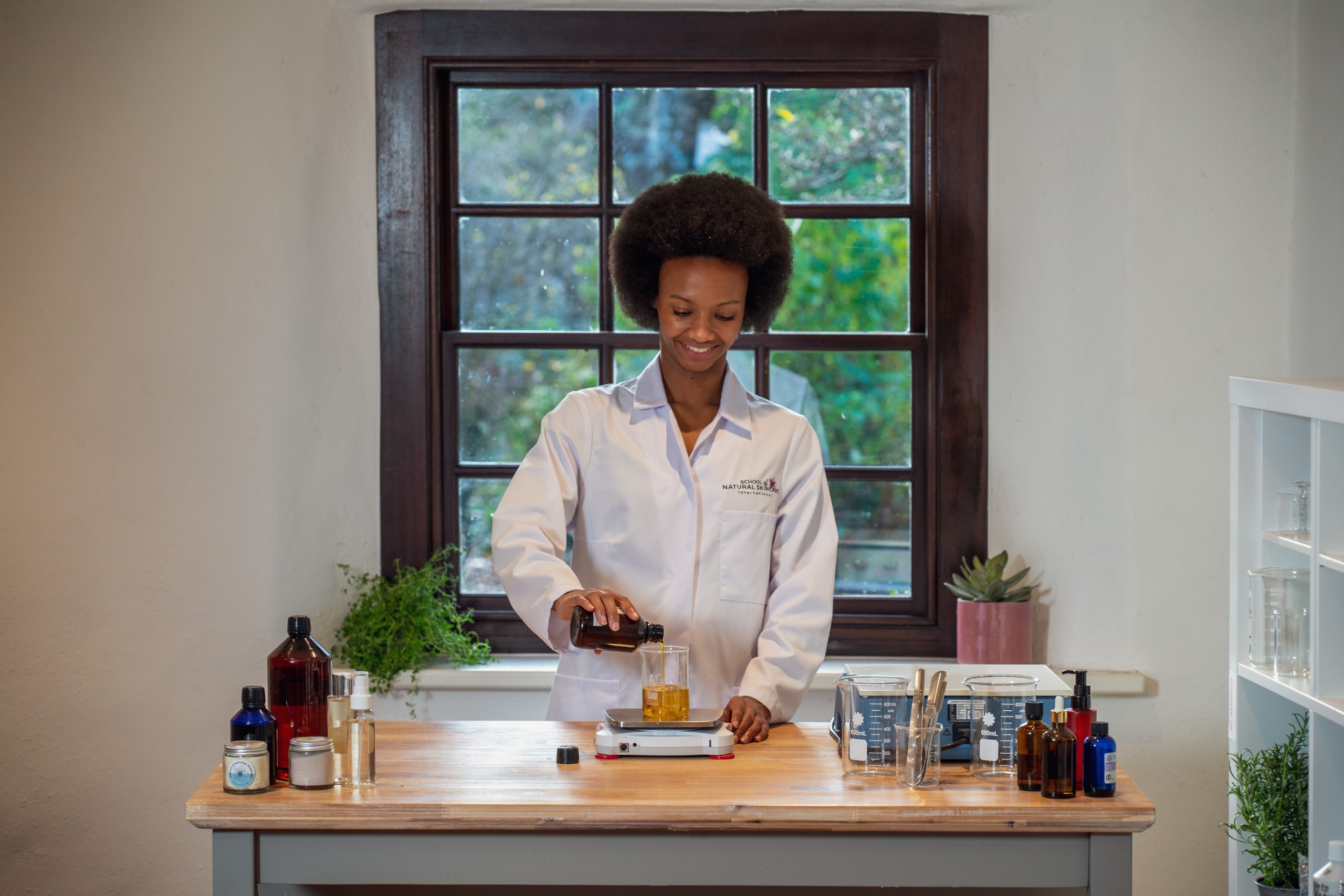 Person in lab coat mixing ingredients at table.