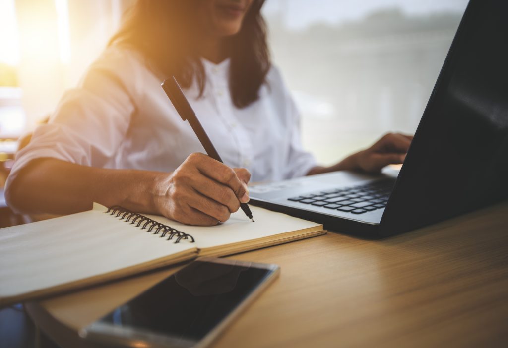 Person writing in notebook, using laptop.