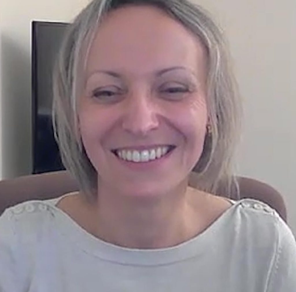 Smiling person sitting indoors with a white sweater.