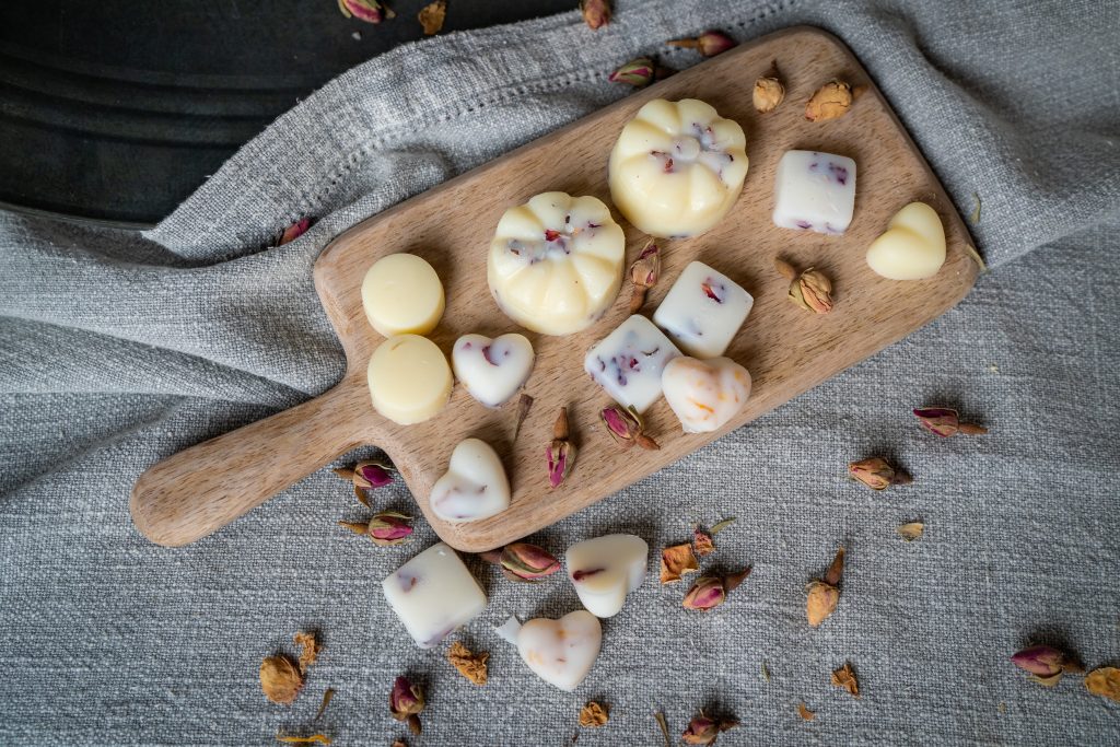 Assorted handmade soaps on wooden board with petals.