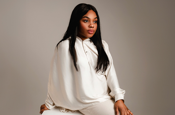 Woman in white outfit sitting against gray background.