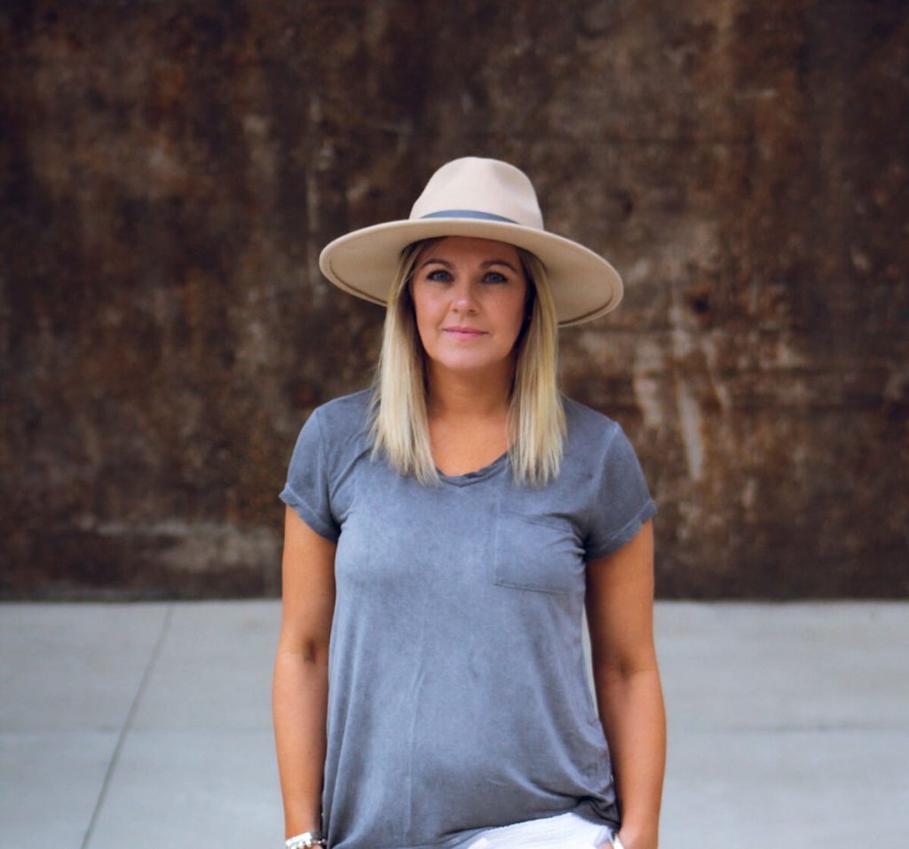 Woman in wide-brimmed hat, casual gray shirt.