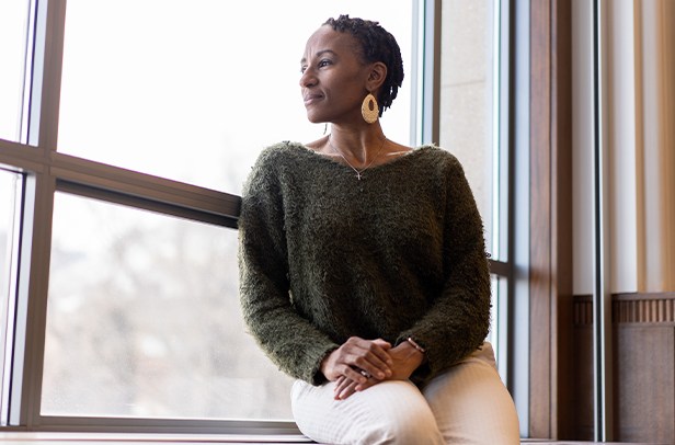 Woman sitting by window, looking outside thoughtfully.