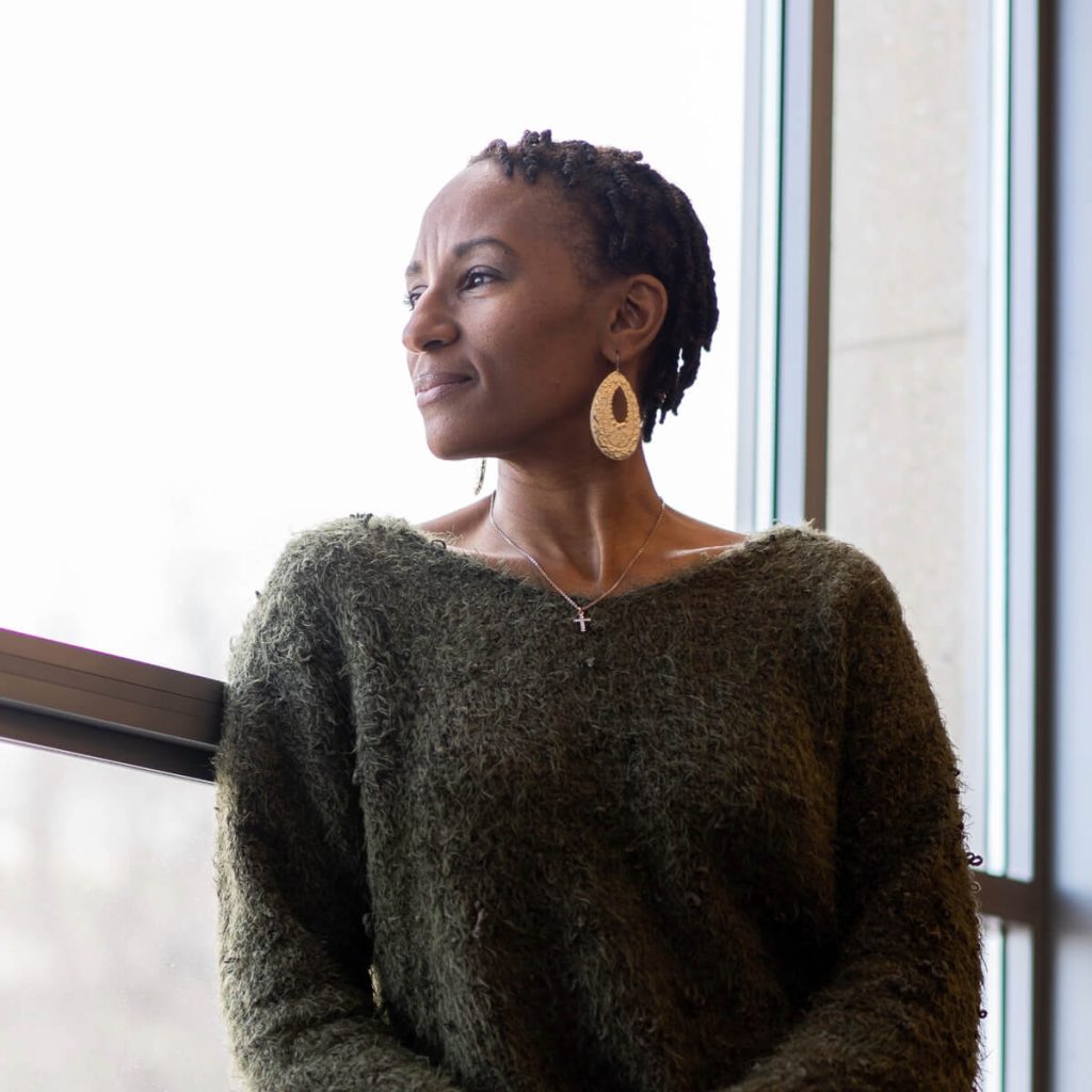 Woman looking out window, wearing textured green sweater.