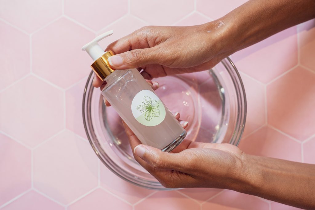 Hands holding a skincare pump bottle over bowl.