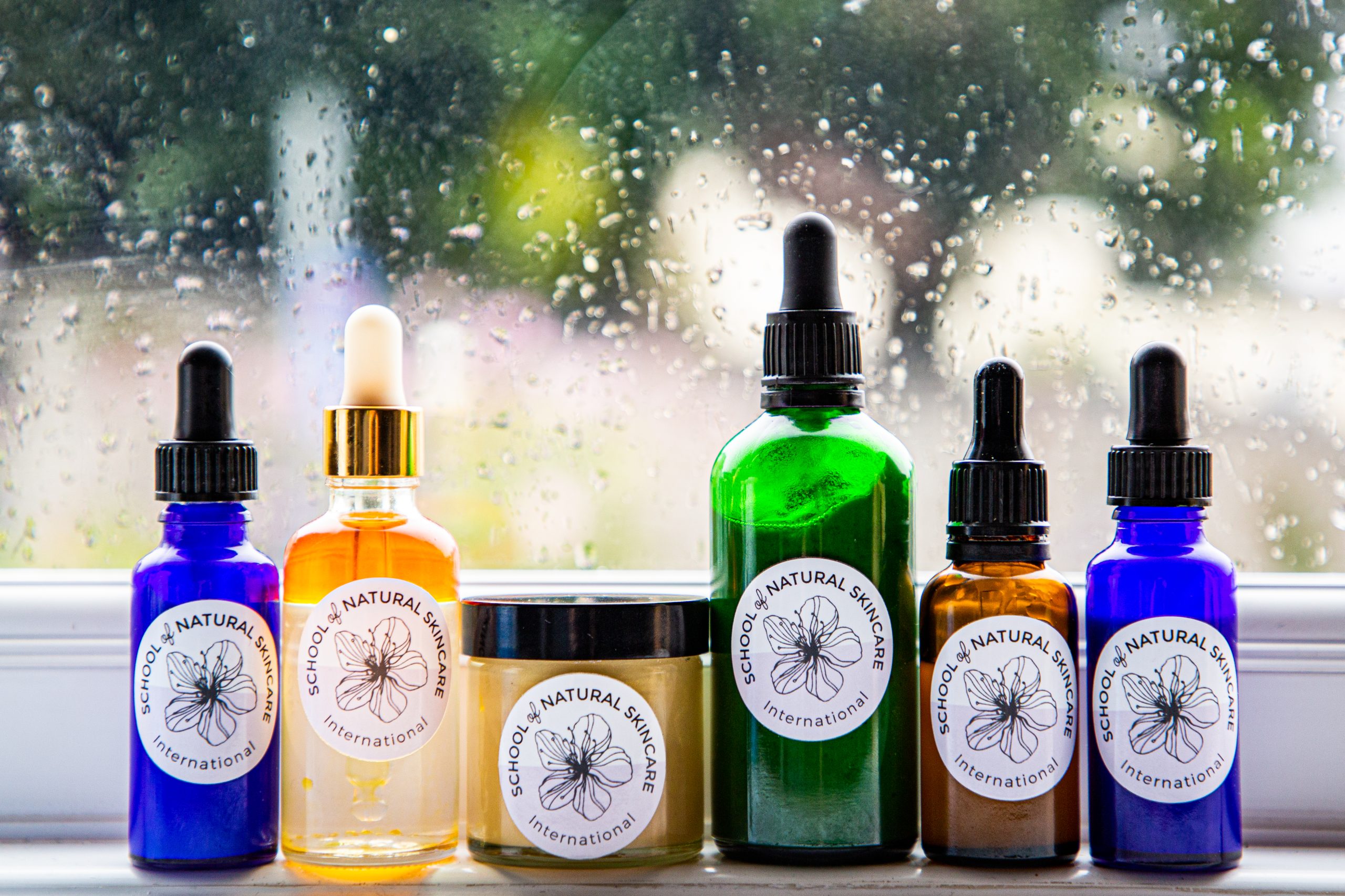 Colorful skincare bottles on rainy window ledge.