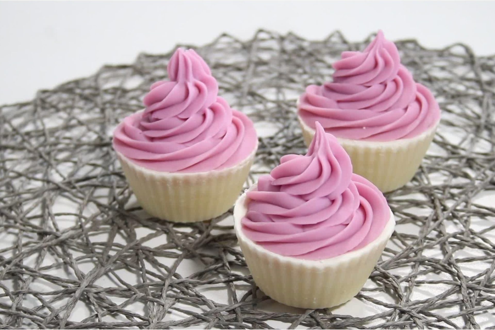 Three cupcakes with pink frosting on decorative mat.